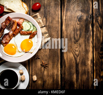 Fresh Breakfast with Cup of coffee, fried bacon with eggs and tomatoes. On a wooden table. Stock Photo