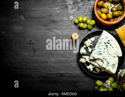 Blue cheese, olives and white grapes. On a black wooden background. Stock Photo