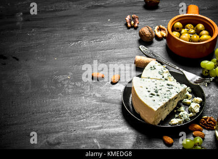 Blue cheese, olives and white grapes. On a black wooden background. Stock Photo