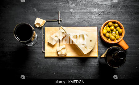 Bottle of red wine with a slice of cheese and on the Board. On a black wooden background. Stock Photo