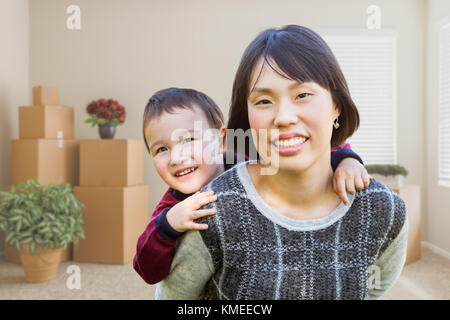 Chinese Mother and Mixed Race Child Inside Empty Room with Moving Boxes and Plants. Stock Photo