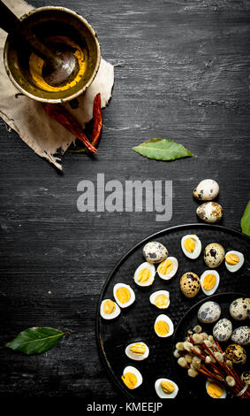 Boiled quail eggs in the willow branches in the ground spices in a mortar.On a black wooden background. Stock Photo