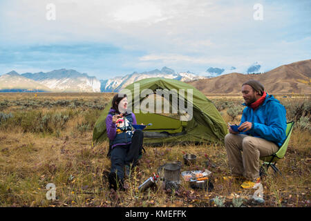 Couple eating while camping in front of tent with mountains of Teton Range in background,Jackson,Wyoming,USA Stock Photo