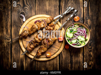 Kebab with fresh salad of cucumbers and onions. On wooden background. Stock Photo