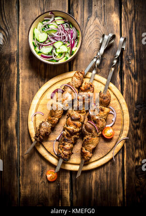 Kebab with fresh salad of cucumbers and onions. On wooden background. Stock Photo