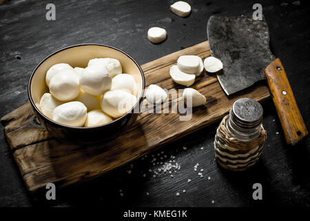 Fresh mozzarella with a hatchet for cutting. On a black wooden background. Stock Photo
