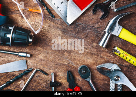 Top view of Working tools,wrench,socket wrench,hammer,screwdriver,plier,electric drill,tape measure,machinist square and safety glasses on wooden back Stock Photo