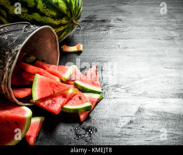 Chopped pieces of watermelon in an old pot. On the black wooden table. Stock Photo