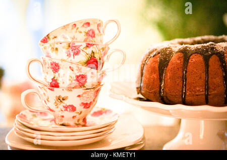 Round Cake With Chocolate Glaze On White Stand With Tea Cups In Roses Stock Photo