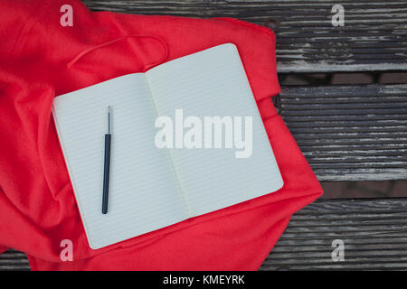 Blank Notepad with a black pen lying on a red blanket. Dark wooden background. Stock Photo