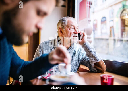 Senior father with smartphone and young son in a cafe. Stock Photo