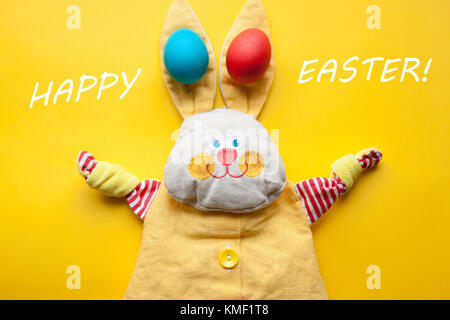 Easter decorations from a handmade toy rabbit and colorful eggs on an orange background. With the words happy Easter. Stock Photo