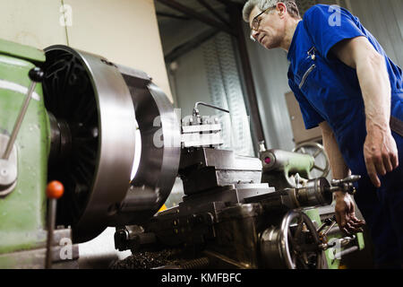 Worker in uniform operating in manual lathe in metal industry factory Stock Photo