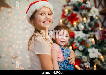 Photo of two sisters in Santa caps on background of New Year's decorations Stock Photo
