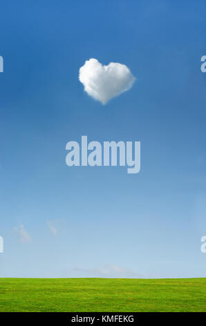 Heart shaped fluffy white cloud set in a bright blue sky with green grass countryside landscape below. Stock Photo