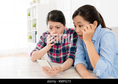 pretty beautiful sisters using mobile cell phone browsing online website information together and finding bad news feeling shocked. Stock Photo