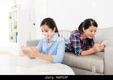 cheerful pretty girls using personal mobile smartphone relaxing in living room at home. Stock Photo
