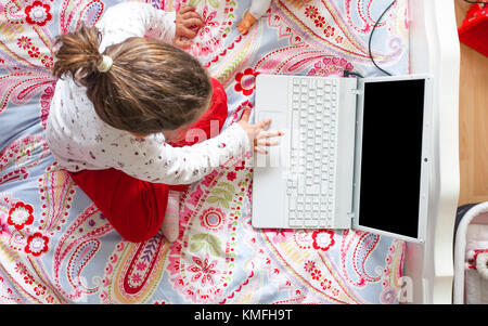Little girl sitting in bed and playing online games in her bedroom. High angle view Stock Photo