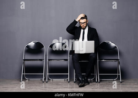 Young man in suit sitting on chair with laptop and waiting for job interview Stock Photo