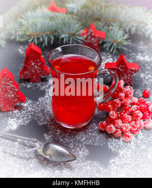 tea made from fresh berries of viburnum in a glass cup and fresh bunch of viburnum with red berries among the Christmas decor, vintage toning
