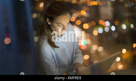 Serious, focused businesswoman working late at laptop in office window at night Stock Photo
