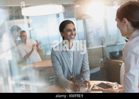 Smiling businesswomen talking, using digital tablet in conference room meeting Stock Photo
