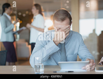 Tired, stressed businessman using digital tablet in conference room Stock Photo