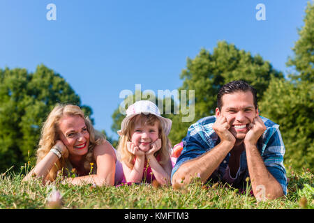 Family lying on meadow, looking to camera, cupping chins in hands Stock Photo