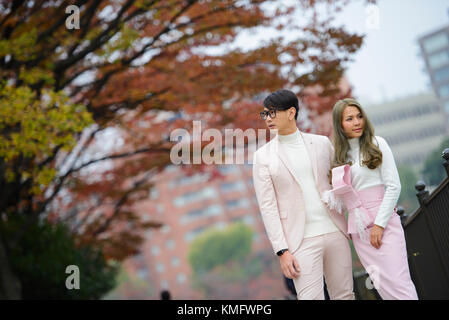 Young japanese couple in love stand together under autumn trees Stock Photo