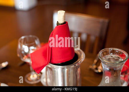 bottle of wine with cork wrapped in red napkin on a table with glasses Stock Photo
