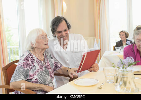 Caretaker reading a book with senior woman at rest home Stock Photo