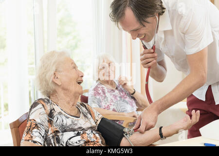 Caretaker checking blood pressure of senior woman in rest home Stock Photo