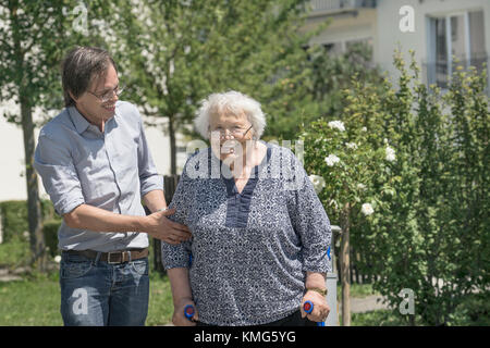 Son walking with disabled mother on crutches Stock Photo