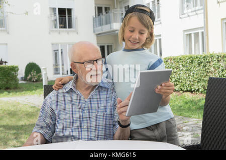 Senior man with grandson using digital tablet in yard of rest home Stock Photo