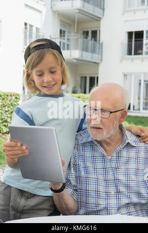 Senior man with grandson using digital tablet in yard of rest home Stock Photo