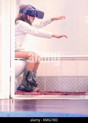 Girl sitting on toilet bowl and wearing virtual reality glasses Stock Photo