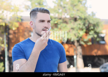 Portrait of young latin man sending voice messages. Outdoors. Urban scene. Stock Photo