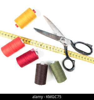 Sewing thread coil with old metal scissors and yellow measuring tape on white background Stock Photo