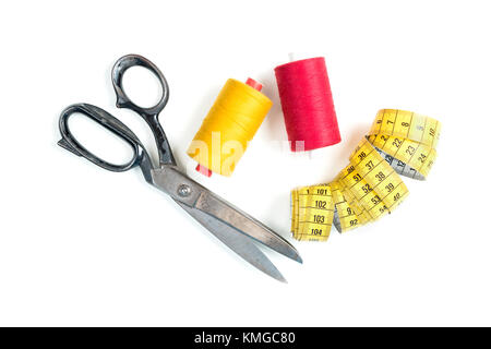Sewing thread coil with old metal scissors and yellow measuring tape on white background Stock Photo