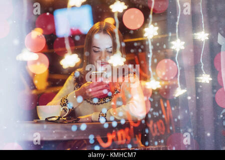 Young beautiful woman sitting in cafe, drinking coffee. Magic snowfall effect. Christmas, new year, Valentines day, winter holidays concept. The photo Stock Photo