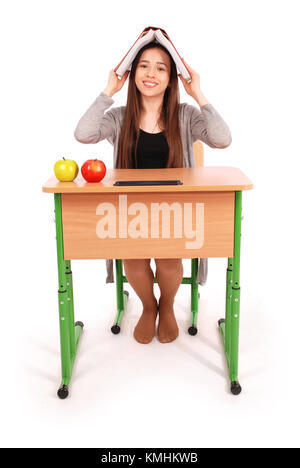 Education, people, teenager and school concept -  teenager school girl sitting at table with a book on her head isolated on white Stock Photo