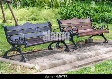 Double metal bench on the block tile floor near the brick pavement in the urban park. Stock Photo