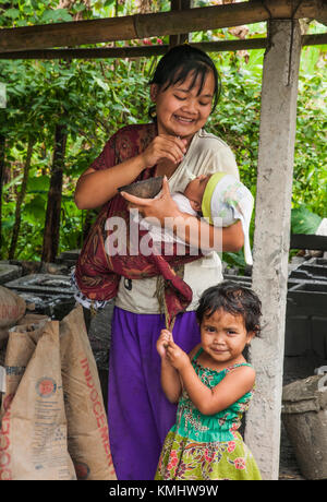 Woman with daughter feeding her baby from a coconut shell in the village of  Tegalalang, Gianyar, Bali, Indonesia. Stock Photo