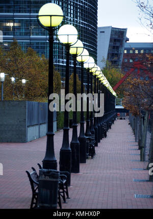 a receding line of globe street lights shining brightly at dusk on the pedestrianized quayside at Salford Quays Salford, Manchester,UK Stock Photo