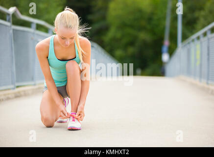 Young woman runner tying shoelaces on bridge Stock Photo
