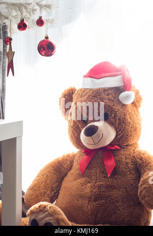 Teddy bear toy with Red Santa hat sitting under christmas tree ornaments Stock Photo