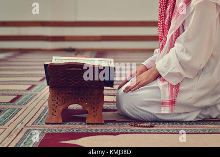 An open Holy quran with wood stand with praying people in background Stock Photo