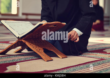 An open Holy quran with wood stand with praying people in background Stock Photo