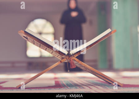 An open Holy quran with wood stand with praying people in background Stock Photo