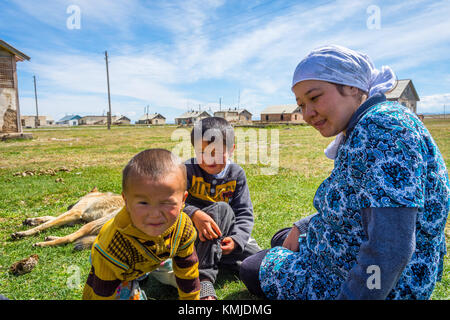 KEL-SUU, KYRGYZSTAN - AUGUST 13: Woman sitting in a grass with her two kids and a dog in a remote Kyrgyz village. August 2016 Stock Photo